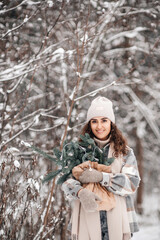 A stylish young woman in a hat stands in a snowy forest with branches of fir nobilis in a craft package