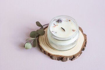 Handmade candle from paraffin and soy wax in glass with wooden wick and dry herbal isolated on pastel pink background. Flat lay, top view, copy space