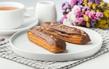 Eclairs with custard and chocolate icing on a white plate. Eclairs with cream filling covered with...