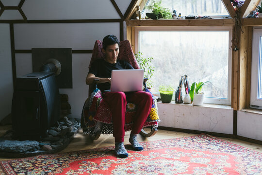 Freelancer guy sitting in rocking chair working on laptop at vintage style home