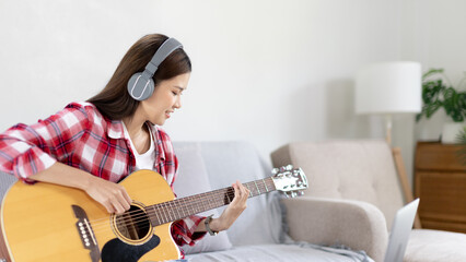 Woman artist playing the guitar and live or stream on laptop in the living room, Relaxation with...