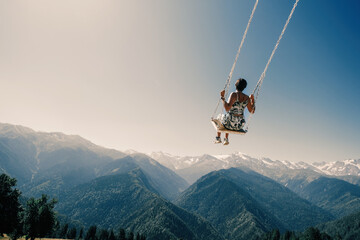 Fototapeta na wymiar Dream and travel concept, Young beautiful woman happy on swing flying in the sky over stunning mountain view