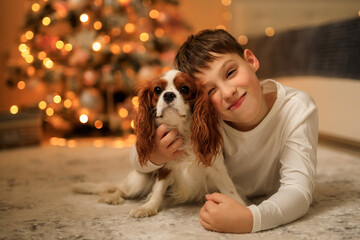 Happy New Year! a boy in light homemade pajamas hugs his pet cavalier king charles spaniel at home...