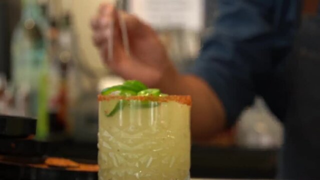 Bartender putting slices of jalapeno pepper in a mango jalapeno margarita drink in a bar