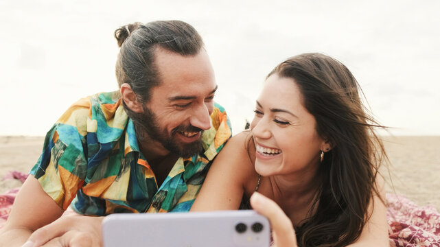 Couple in love relaxing on the beach, watching videos and photos on mobile phone
