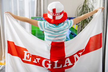 Fototapeta premium A boy holding England flag and watching soccer game on TV at home