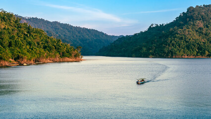 VIew of long-tailed boat floating on blue river in mountain with green forest. River in Khun Dan Prakan Chon Dam in Thailand. Landscape. Tourists on a boat to enjoy scenery in evening. Tourism concept