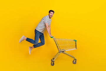 Full length photo of shiny impressed man wear white t-shirt jumping high buying supermarket food isolated yellow color background - obrazy, fototapety, plakaty