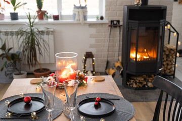 Festive interior of house is decorated for Christmas and New Year in loft style with black stove, fireplace, Christmas tree. Warm studio room with set table, burning wood, cozy and heating of home