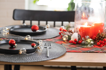 Obraz na płótnie Canvas Festive table set in the living room for Christmas and New year in loft style. Christmas tree, black plates and forks, woven napkins, trendy tableware, cozy interior of the house