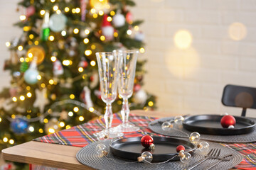 Festive table set in the living room for Christmas and New year in loft style. Christmas tree, black plates and forks, woven napkins, trendy tableware, cozy interior of the house