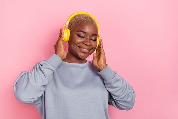 Portrait of positive adorable girl closed eyes hands touch headphones enjoy new single isolated on pink color background