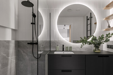 Modern minimalistic bathroom interior design with grey stone tiles, black furniture, eucalyptus in...
