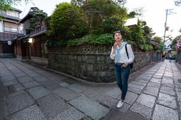 Fototapeta na wymiar full length of lost asian Japanese female traveler looking around surroundings with hand on chin at the corner of rock pavement during her visit at Ninenzaka and Sannenzaka in Kyoto japan