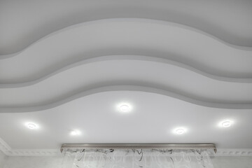 suspended ceiling with halogen spots lamps and drywall construction  with intricate crown molding in empty room in apartment or house. Stretch ceiling white and complex shape. - obrazy, fototapety, plakaty