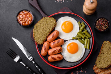 Tasty English breakfast of fried eggs, beans, asparagus, sausages with spices and herbs