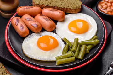 Tasty English breakfast of fried eggs, beans, asparagus, sausages with spices and herbs