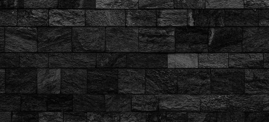 Dark and scary black stone wall background. Panoramic view of a wide empty old black block stone wall texture 