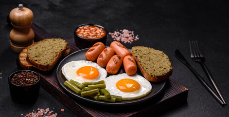 Tasty English breakfast of fried eggs, beans, asparagus, sausages with spices and herbs