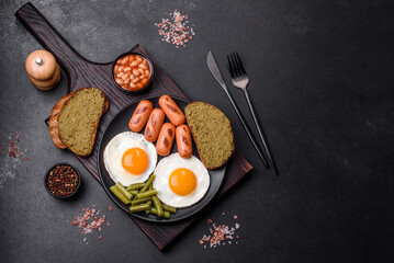 Tasty English breakfast of fried eggs, beans, asparagus, sausages with spices and herbs