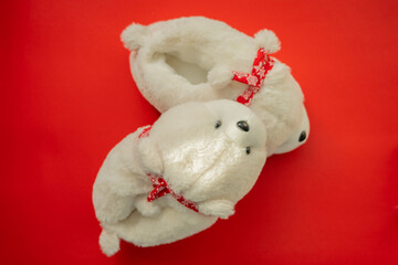 Warm polar bear slippers with Christmas ribbon on a red background. New Year's mood. Beautiful home slippers. Comfort. Top view. Close-up. 