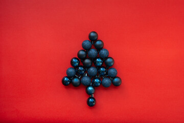 Christmas tree balls laid out in the shape of a Christmas tree. Dark blue Christmas tree balls on a red background. Glossy, matte and glitter Christmas ornaments. Christmas decorations. 