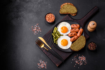 Tasty English breakfast of fried eggs, beans, asparagus, sausages with spices and herbs