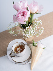 Artistic still life with a bouquet of pink peonies and a cup of tea. Pink peony flower in a horn. Flowers for design. Vertical photo.