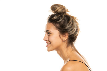 smiling woman with messy loose bun and no makeup on a white studio background. side profile view