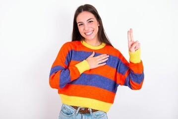 Young caucasian woman wearing colorful knitted sweater over white background smiling swearing with hand on chest and fingers up, making a loyalty promise oath.