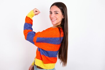 Portrait of powerful cheerful Young caucasian woman wearing colorful knitted sweater over white background showing muscles.