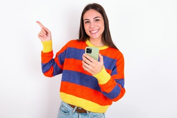 Wow!! excited Young caucasian woman wearing colorful knitted sweater over white background showing mobile phone with open hand gesture