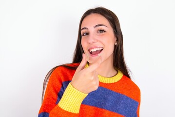 Young caucasian woman wearing colorful knitted sweater over white background holding an invisible aligner ready to use it. Dental healthcare and confidence concept.