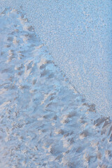 snow frost in the form of natural patterns on the window pane against the background of the morning sky