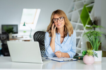 Attractive blond haired business woman using laptop and smartphone the office