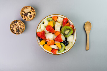 Fresh fruit salad in a bowl. Multicolored and tropical fruits. Pineapple, mango, grape, strawberry, papaya, melon, kiwi. Additional with chestnuts and granola. Top view. Selective focus