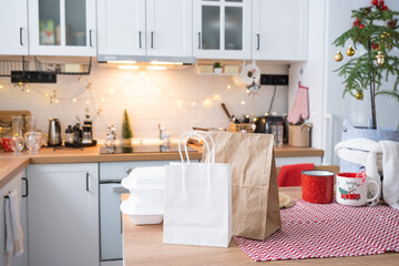 Food delivery service containers on table white scandi festive kitchen in christmas decor. Eve New year, saving time, too lazy to cook, hot order, disposable plastic box in fairy light. mock up