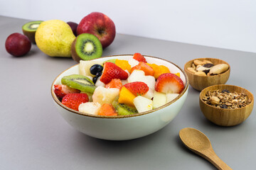 Fresh fruit salad in a bowl. Multicolored and tropical fruits. Pineapple, mango, grape, strawberry, papaya, melon, kiwi. Additional with chestnuts and granola. Selective focus