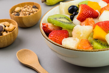 Fresh fruit salad in a bowl. Multicolored and tropical fruits. Pineapple, mango, grape, strawberry, papaya, melon, kiwi. Additional with chestnuts and granola. Selective focus