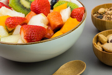 Fresh fruit salad in a bowl. Multicolored and tropical fruits. Pineapple, mango, grape, strawberry, papaya, melon, kiwi. Additional with chestnuts and granola. Selective focus
