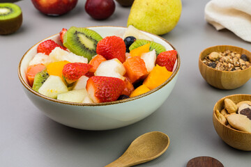 Fresh fruit salad in a bowl. Multicolored and tropical fruits. Pineapple, mango, grape, strawberry, papaya, melon, kiwi. Additional with chestnuts and granola. Selective focus
