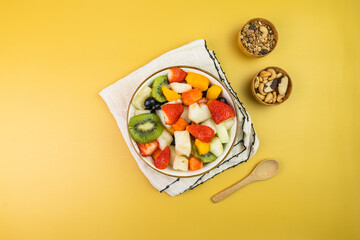 Fresh fruit salad in a bowl. Multicolored and tropical fruits. Pineapple, mango, grape, strawberry, papaya, melon, kiwi. Additional with chestnuts and granola. Top view. Selective focus
