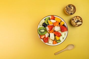 Fresh fruit salad in a bowl. Multicolored and tropical fruits. Pineapple, mango, grape, strawberry, papaya, melon, kiwi. Additional with chestnuts and granola. Top view. Selective focus
