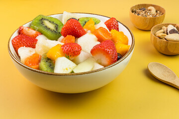 Fresh fruit salad in a bowl. Multicolored and tropical fruits. Pineapple, mango, grape, strawberry, papaya, melon, kiwi. Additional with chestnuts and granola. Selective focus