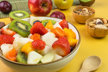 Fresh fruit salad in a bowl. Multicolored and tropical fruits. Pineapple, mango, grape, strawberry, papaya, melon, kiwi. Additional with chestnuts and granola. Selective focus