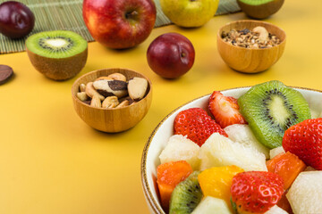 Fresh fruit salad in a bowl. Multicolored and tropical fruits. Pineapple, mango, grape, strawberry, papaya, melon, kiwi. Additional with chestnuts and granola. Selective focus