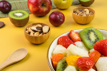 Fresh fruit salad in a bowl. Multicolored and tropical fruits. Pineapple, mango, grape, strawberry, papaya, melon, kiwi. Additional with chestnuts and granola. Selective focus