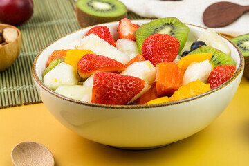 Fresh fruit salad in a bowl. Multicolored and tropical fruits. Pineapple, mango, grape, strawberry, papaya, melon, kiwi. Additional with chestnuts and granola. Selective focus