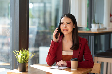 Attractive and attractive young Asian businesswoman is using phone to talk to customers and using laptop for work happily.