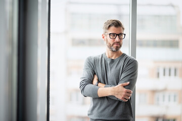 Fototapeta premium Confident businessman with arms crossed standing at the office